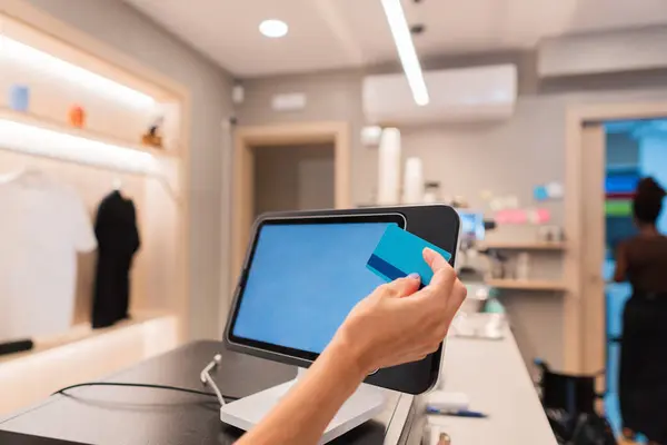 Satıcı kadın elinde bir kredi kartı tutuyor, modern bir butikte bağlantısız bir ödeme yapıyor.