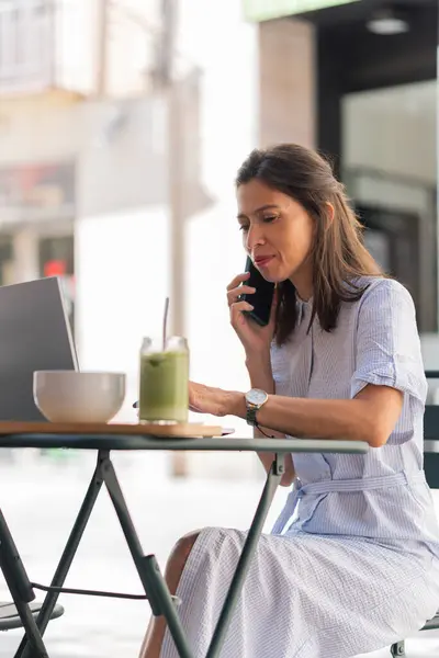 İş kadını laptopuyla uzaktan çalışırken ve telefonla konuşurken sağlıklı bir kahvaltıdan zevk alıyor.