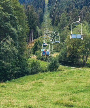 Cable car, ski lift with blue seats in summer among the green pine trees