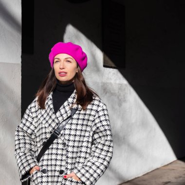 beautiful brunette in a pink beret and checkered coat walks around town