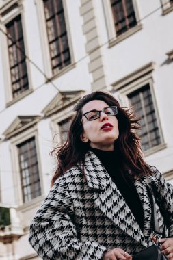 Pembe bereli ve kareli kaz ayağı paltolu güzel esmer duvarda duruyor.