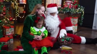 Mariupol, Ukrayna - 12.10.2021: Mutlu anne ve kız Noel Baba ile oturuyor ve Noel ağacı yakınında renkli süslemelerle oynuyorlar. Yüksek kaliteli FullHD görüntüler