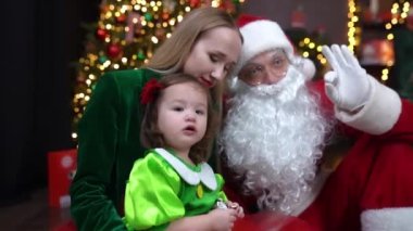 Woman sit with her daughter and Santa Claus in front of Christmas tree in decorated studio, New year footage. High quality FullHD footage