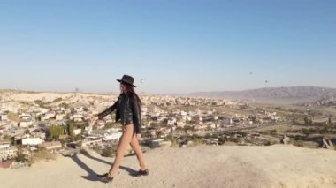 Şapkalı ve siyah ceketli genç bir kadın Kapadokya 'da gün batımına doğru yürüyor, Türk seyahat beldesi, seyahat tutkusu, tatil mutluluğu konsepti. Yüksek kaliteli FullHD görüntüler