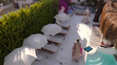 Aerial footage of woman walking on infinity pool edge wearing a beautiful bathrobe in luxury hotel. Turkey hotel. High quality FullHD drone footage