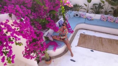 Aerial view of woman in bathrobe sitting and lying in tropical resort or hotel with beautiful flowerbed. High quality FullHD drone footage