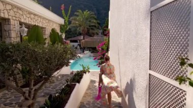 Aerial view if woman walking on infinity pool edge wearing a beautiful bathrobe in luxury hotel. Vacation concept. High quality FullHD drone footage