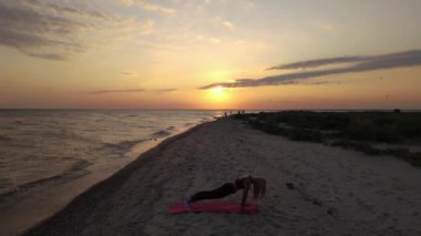 Aktif kadın gün batımında plajda yoga yapıyor. Spor delisi kız deniz kenarında pilates yapıyor, İHA görüntüleri. Yüksek kaliteli FullHD görüntüler