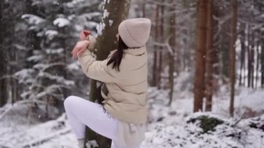Ceketli, şapka takan, gülümseyen ve Avusturya 'nın kış sezonunda güzel donmuş ormanında kameraya bakan tatlı bir kız. Yüksek kalite 4k görüntü