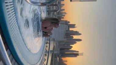 Woman sit in jacuzzi in a roof terrace in Dubai, beautiful view of modern buildings, sunset time, vertical video. High quality FullHD footage