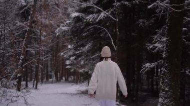 Girl in white jacket and hat walking in forest in winter season, Austria park. High quality 4k footage
