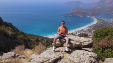 Aerial panoramic view of man sit on the rock shooting himself aerial. Oludeniz beach. High quality 4k footage