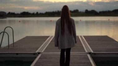 Back view of woman with braids walking on platform, lake, sunset time. High quality 4k footage