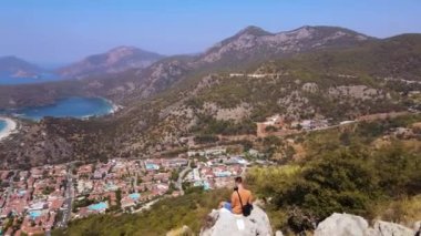 Panoramic view of Oludeniz beach with man sit on the rock, shooting himself aerial background. Amazing beautiful panoramic view from drone of natural park of Oludeniz. High quality 4k footage