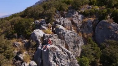 Young man sit on the rock of mountain, shooting himself. Oludeniz beach background. Modern technologies for video filming. Amazing beautiful panoramic view from drone. High quality 4k footage