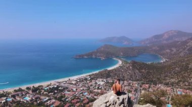Drone back view of man on the rock, Oludeniz beach,, beautiful view. Amazing beautiful panoramic view from drone of natural park of Oludeniz blue lagoon. High quality 4k footage