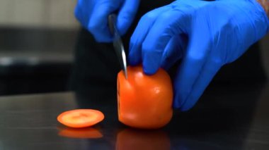 A close-up of cutting a juicy and bright tomato on a table. Blue gloves. High quality FullHD footage