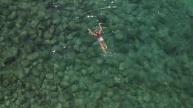 girl in a white bathing suit swims in the mediterranean sea, clear water, a lot of stones. High quality 4k footage