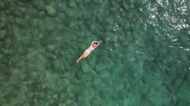 Akdeniz 'de beyaz mayo giymiş bir kadın sırt üstü yüzüyor. Suyun mavi rengi. Yüksek kalite 4k görüntü