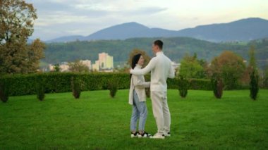 Young couple in white clothes stay mountains background, hug each other and talk. High quality 4k footage