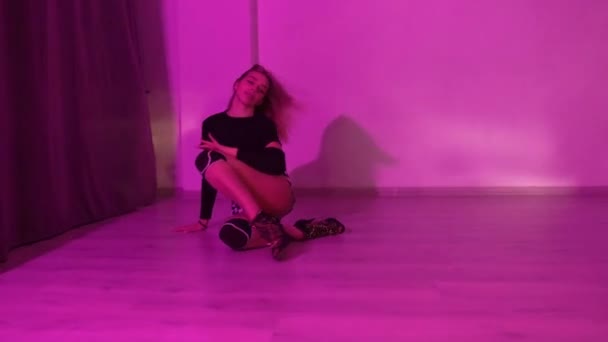 穿着高跟鞋的女孩穿着格子花短裤 跳舞的膝盖垫在地板上跳舞 紫色的灯光照亮着演播室 优质Fullhd影片 — 图库视频影像