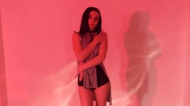 Gri elbiseli, siyah topuklu seksi esmer kız ışıklı stüdyoda yerde dans ediyor. Yüksek kaliteli FullHD görüntüler