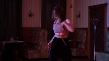 Kamera, gri ve siyah elbiseli seksi kızın ışıklı odada dans edişini, 4K dans görüntülerini çeker. Yüksek kalite 4k görüntü