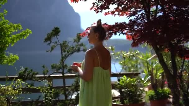 緑のドレスの美しい女性は ハルシュタットの自然景観の中でコーヒーと一緒に滞在します 高品質4K映像 — ストック動画