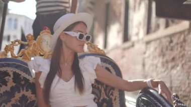 Gözlüklü ve şapkalı bir kız Venedik Kanalı, İtalya 'da gondola biniyor. Yüksek kalite 4k görüntü