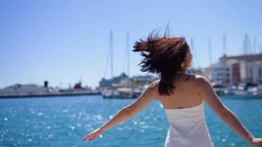 Beyaz elbiseli kız İbiza 'nın rıhtımında dönüyor, güneşli bir gün, mutlu bir kadın. Yüksek kalite 4k görüntü