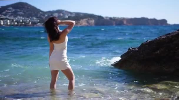 身着白衣的女孩的背影留在海滩的水面上 浪花汹涌 高质量的4K镜头 — 图库视频影像