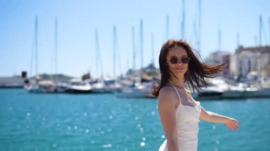 Beyaz elbiseli bir kızın arka manzarası rıhtımda yürüyor, tekne arka planı, İbiza. Yüksek kalite 4k görüntü