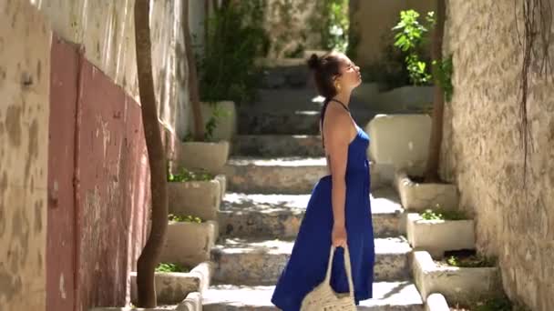 穿着蓝色衣服和太阳镜的女孩走在伊比扎老城区的小巷里探索 高质量的4K镜头 — 图库视频影像