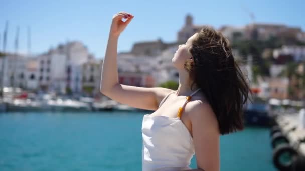 身穿白衣的女孩沿着泊位站在Ibiza海岸的摄像机前摆姿势 高质量的4K镜头 — 图库视频影像