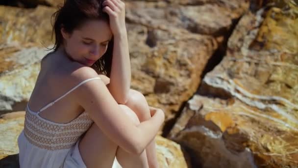 身穿白色衣服的女孩坐在石堤上 微笑着晒太阳 高质量的4K镜头 — 图库视频影像