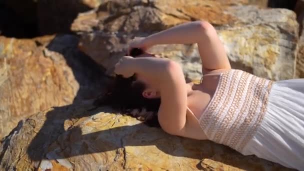 Chica Tumbada Piedra Vestido Blanco Descalza Mira Cámara Sol Sol — Vídeos de Stock