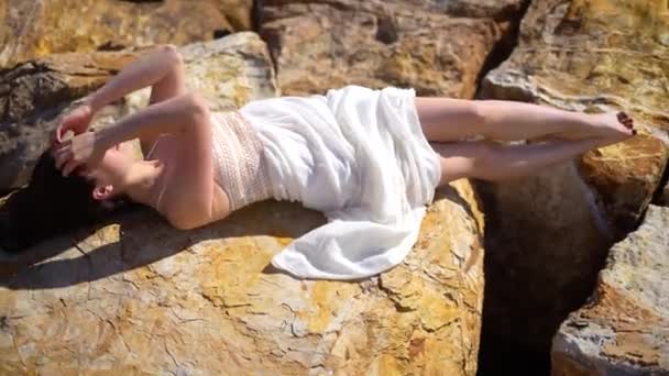 女孩穿着白衣躺在石头上 光着脚 看着相机 晒着太阳 高质量的4K镜头 — 图库视频影像