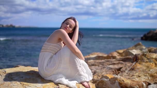 Menina Vestido Branco Sentado Quebra Mar Pedra Olhar Para Câmera — Vídeo de Stock