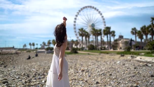 穿着白色衣服的迷人女孩在棕榈树和摩天轮附近旋转 高质量的4K镜头 — 图库视频影像