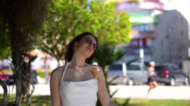 Beyaz elbiseli ve güneş gözlüklü bir kız İbiza caddesinde kameraya poz veriyor. Yüksek kalite 4k görüntü