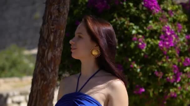 在阳光明媚的伊比萨市 穿着蓝色衣服的格里尔站在花丛旁 高质量的4K镜头 — 图库视频影像