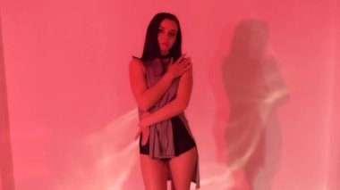 Gri elbiseli, siyah topuklu seksi esmer kız ışıklı stüdyoda yerde dans ediyor. Yüksek kaliteli FullHD görüntüler