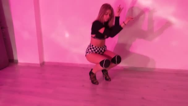 穿着高跟鞋的女孩穿着格子花短裤 舞着膝盖垫 在工作室的红色背光下跳着色情舞 优质Fullhd影片 — 图库视频影像
