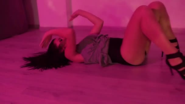 黒いハイヒールを着たセクシーなブルネットの女の子がライトアップされたスタジオで床の上で踊っています 高品質のフルHd映像 — ストック動画