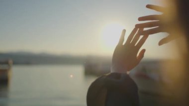 Görüntüde, güneşe doğru uzanan bir çift el, uzanıp uzanmanın bir jestini sembolize ediyor. Sahne, doğayla bir bağlantı hissi veriyor.