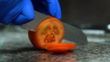 A close-up of cutting a juicy and bright tomato on a table. Blue gloves. High quality FullHD footage