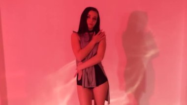 Gri elbiseli, siyah topuklu seksi esmer kız ışıklı stüdyoda yerde dans ediyor. Yüksek kaliteli FullHD görüntüler