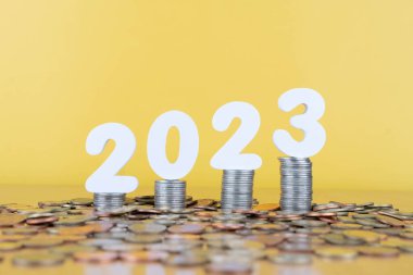 2023 Yeni Yıl Tasarruf ve Finansal Planlama. 2023 numaralı madeni para yığını altın arka planda ahşap masanın üzerinde. Ticari büyüme, yatırım, kâr ve bankacılık için yaratıcı bir fikir.