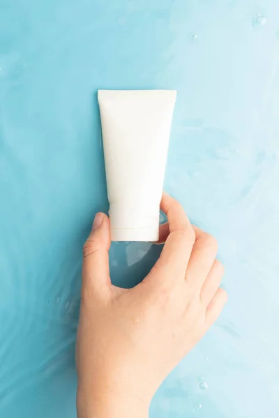 Female Hand Holding Blank White Squeeze Tube Blue Water Surface — Stock Photo, Image