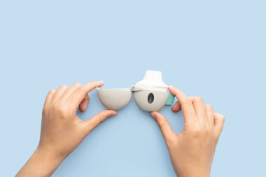 Astım ve KOAH konsepti. Mavi arka planda Tiotropium bromür spreyini tutan kadın eli. Akciğer iltihabı tedavisi ve astım krizini önlemek için bronkodilatörden oluşan bir ilaç cihazı..